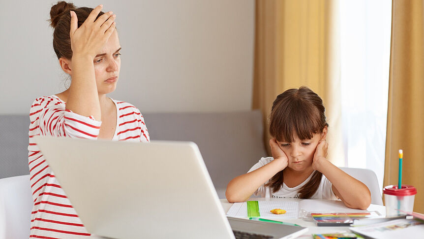 Mutter und Tochter sitzen vor den Schulaufgaben und einem PC am Arbeitstisch und scheinen verzweifelt zu sein.