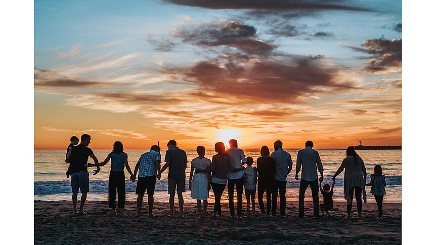 Eine Gruppe von Menschen am Strand, die einem Sonnenuntergang zugewandt sind.