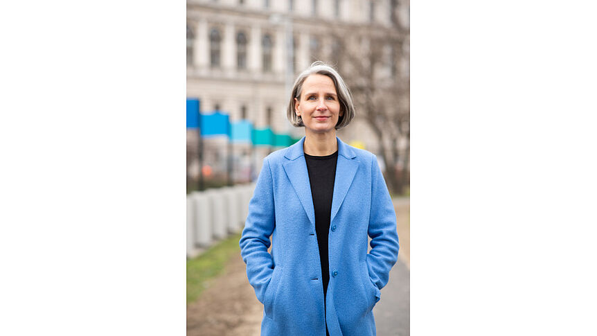 Ulrike Zartler steht an einem Spielplatz in blauer Jacke