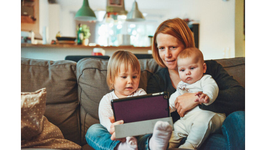 Mutter sitzt mit zwei Kleinkindern und Ipad auf der Couch