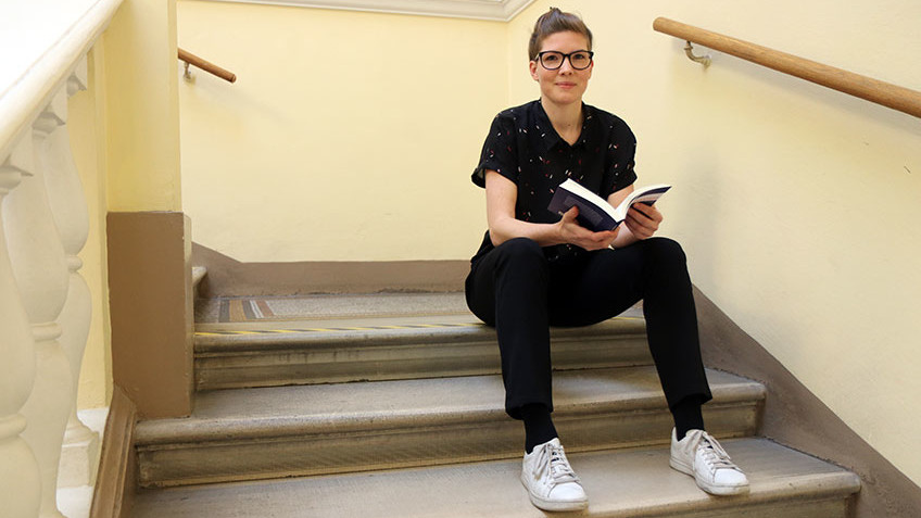 Carina Altreiter sitzt mit ihrem neuen Buch auf den Stufen des Stiegenhauses von Rooseveltplatz 2